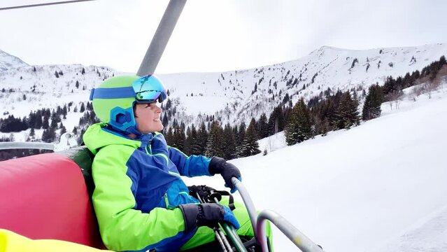 Boy sit in sport outfit with helmet on ski chair lift