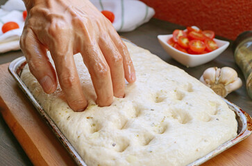 Using fingertips to create dimples in the dough for baking Italian Focaccia Genovese bread