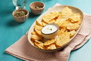 An oval plate with cheese tortilla chips and a yoghurt dip on a blue wooden surface