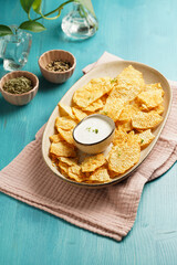 An oval plate with cheese tortilla chips and a yoghurt dip on a blue wooden surface