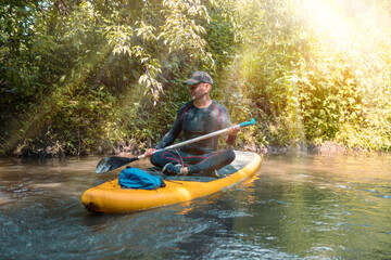 Beautiful view. A trip on a SAP board. A narrow river in the middle of the forest, an extreme route. bag with water protection. Tours and tourism, active recreation. sun rays are shining. Senior man