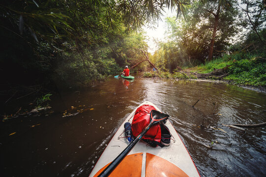 View from the first person. A trip on a SAP board. A narrow river in the middle of the forest, an extreme. Red waterproof bag. Tours and tourism, active recreation. the sun's rays are shining