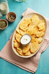 An oval plate with cheese tortilla chips and a yoghurt dip on a blue wooden surface