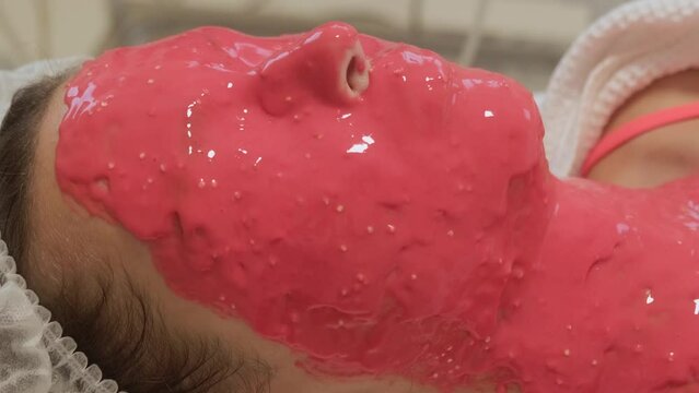 Red alginate mask on woman's face, close-up. Facial skin care concept. Relaxing anti-aging procedures in beauty salon.