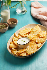 An oval plate with cheese tortilla chips and a yoghurt dip on a blue wooden surface