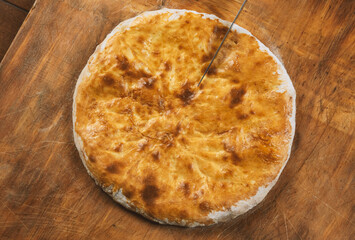 Person cutting  homemade cheese pie on wooden background. Bulgarian banitsa, Georgian khachapuri, Greek tiropita