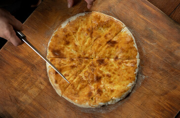 Person cutting  homemade meat pie on wooden background. Bulgarian banitsa, Georgian khachapuri, Greek tiropita