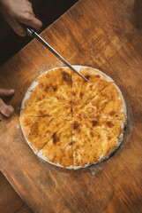 Person cutting  homemade cheese pie on wooden background. Bulgarian banitsa, Georgian khachapuri, Greek tiropita