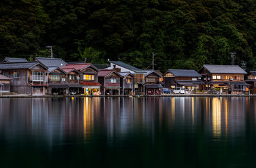 Traditional wooden boathouses reflect of calm water as night falls on Ine, Kyoto