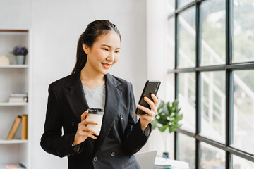 Young Happy Asian business female standing and using mobile smartphone in office room workplace.