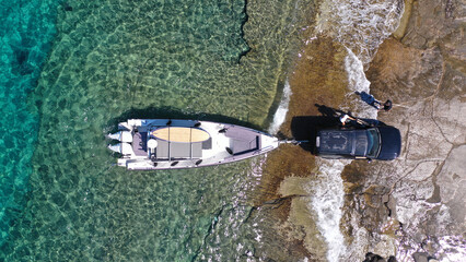 Aerial top view photo of speed boat on transport trailer being towed by truck from emerald sea...