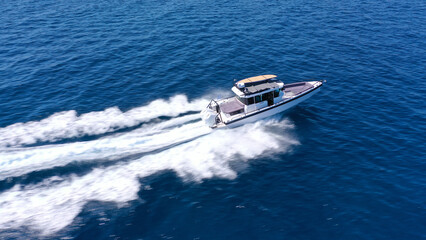 Aerial drone photo of small speed boat with dual outboards cruising in high speed deep blue Aegean sea