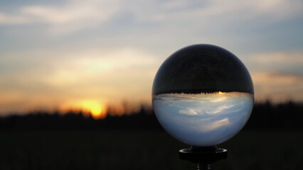 Fototapeta na wymiar Rural landscape. Spherical lens (crystal ball) and colorful sunset against the background of the forest. Leningrad region, Russia.
