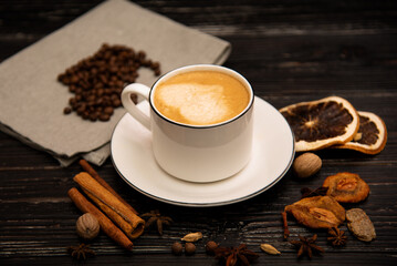 A mug of coffee on a wooden background with spices.