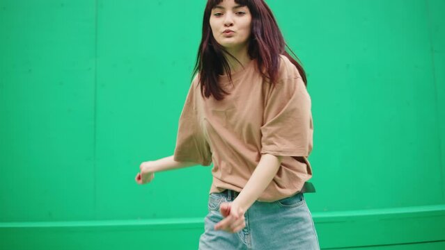 Young woman dancing hip hop on green background wall. Modern dance choreography. Female professional dancer showing dance movings. Musical video.