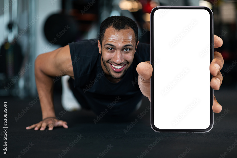 Wall mural fitness offer. sporty black man showing blank smartphone while doing push-ups