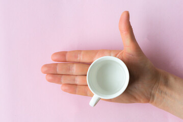 An empty coffee cup in a woman's palm. Top view of human hand on pink background