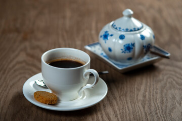 a cup of coffee with cookies and a sugar bowl on the table