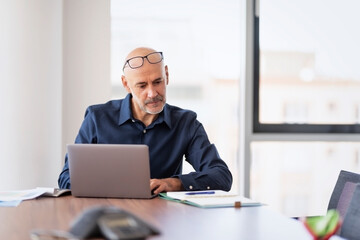 Businessman looking thoughtfully while sitting at the office and working on laptop