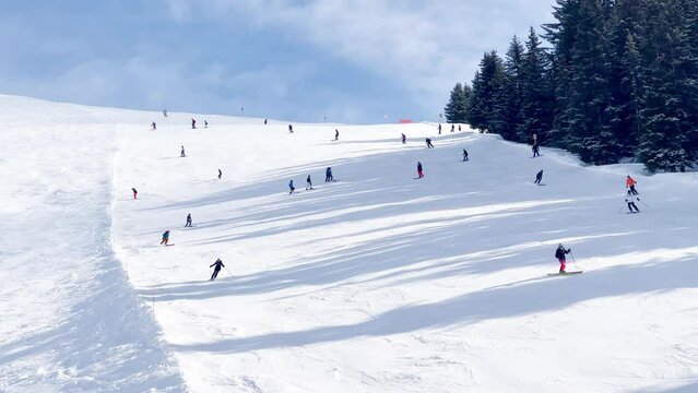 Skiers on alpine ski resort go down the slope view from above