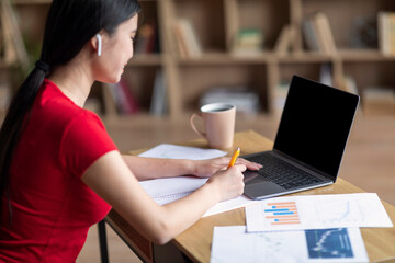 Glad teen chinese girl student in headphones study with laptop with empty screen watch video lesson