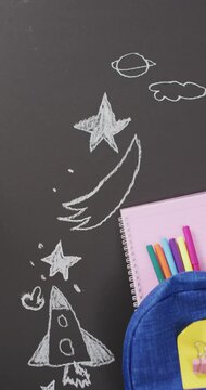 Vertical video of schoolbag and school stationery with chalk drawings on black background