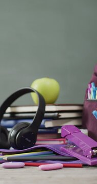 Vertical video of headphones, schoolbooks and apple on desk with chalk board in background