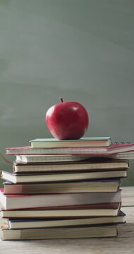 Vertical video of apple on pile of schoolbooks on desk with chalk board in background