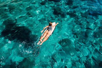 Fototapeta na wymiar Surfer girl rowing on surfboard in transparent turquoise ocean. Aerial view with surfer