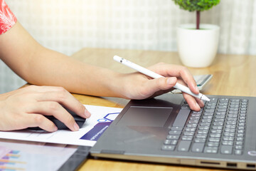 Closeup of female hand holding a pen and typing on a computer keyboard.