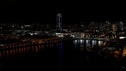 Fototapeta na wymiar The view from the drone.Stock footage.A beautiful city at night located next to the river and beautiful high-rise new buildings and offices and with a calm illuminated road