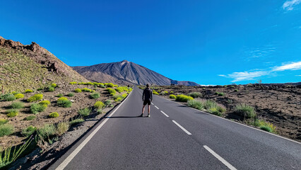 Tourist man standing on scenic mountain road leading to volcano Pico del Teide, Mount El Teide National Park, Tenerife, Canary Islands, Spain, Europe. Road trip on a sunny summer day. Freedom vibes