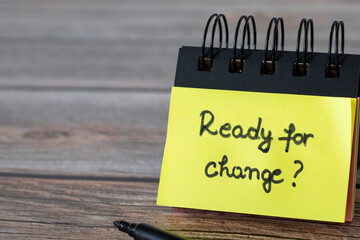 Ready for change, a handwritten message on a yellow note written in a small spiral notebook and a black marker on a wooden table. A close-up.