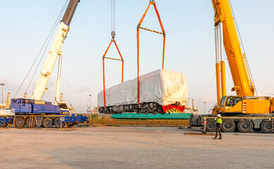 Mobile crane lifting new electric diesel locomotive On the truck, waiting to be lifted onto the rails at the port  using  2 cranes lifting diesel-electric locomotives
