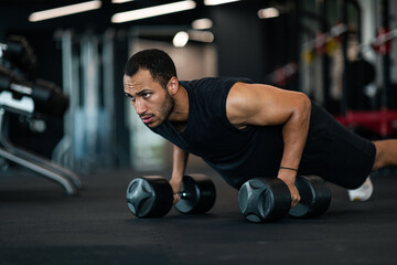 Fototapeta na wymiar Muscular Black Man Making Dumbbell Push-Ups Exercise At Gym