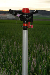 Close-up and low key vertical photograph of a sprinkler on farmland at sunset. Selective focus. Background blurred.