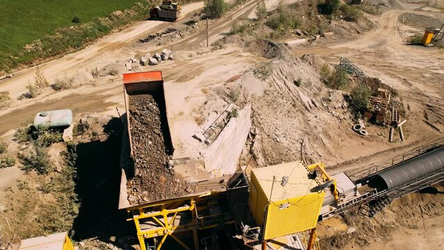 Quarry dump truck unloads the rock into a rock crusher. Open pit mine quarrying extractive industry stripping work. Conveyor and production of construction gravel and sand.