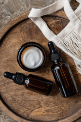 Set of natural organic SPA beauty products on wooden tray. ymoisturizer cream jar, amber glass pipette bottle, cotton besh bag on wooden board.