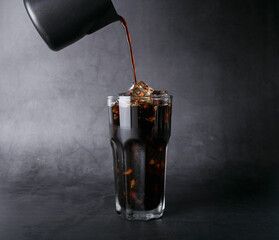 Poured coffee of ice americano coffee into a transparent glass on  black background studio photo