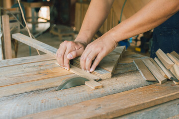 Asian carpenter is using a circular saw to cut wood to construct a storage box on a desk table at his factory. Working as your own boss at home concept