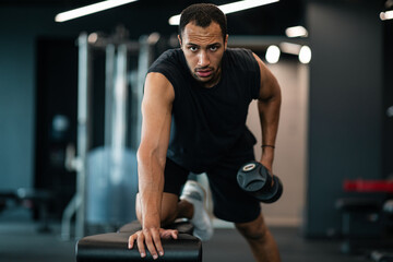 Muscular african american man doing biceps workout with dumbbell in gym