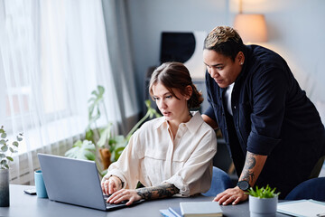 Portrait of two women using laptop while working in small company office, copy space