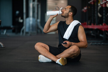 Young Black Male Athlete Drinking Water While Relaxing After Training At Gym