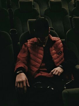 A Guy In A Red Jacket And A Black Cap In A Leather Armchair In A Movie Hall