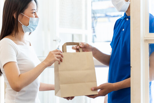 Young Asian woman wearing face mask receiving food and drink package from delivery service company staff at home for prevent coronavirus infection, Food delivery during covid-19 outbreak.
