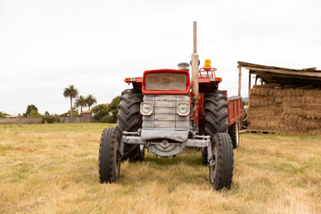 Obraz premium Front view of a tractor standing in a crop field. The day is cloudy. Concept of agriculture and rural life.