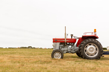 Side view of a tractor standing in a crop field. The day is cloudy. Concept of agriculture and rural life. Space for text.