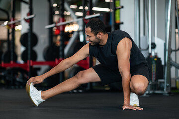 Obraz na płótnie Canvas Sporty Young Black Man Stretching Leg Muscles While Training At Gym