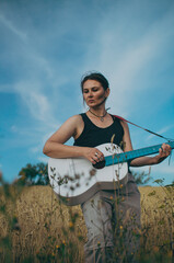 Beautiful girl in a wheat field in August with a white guitar with a blue fretboard against a blue summer sky

