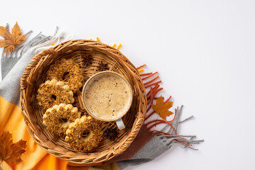 Autumn mood concept. Top view photo of wicker basket with cup of frothy cocoa cookies anise fallen maple leaves and scarf on isolated white background